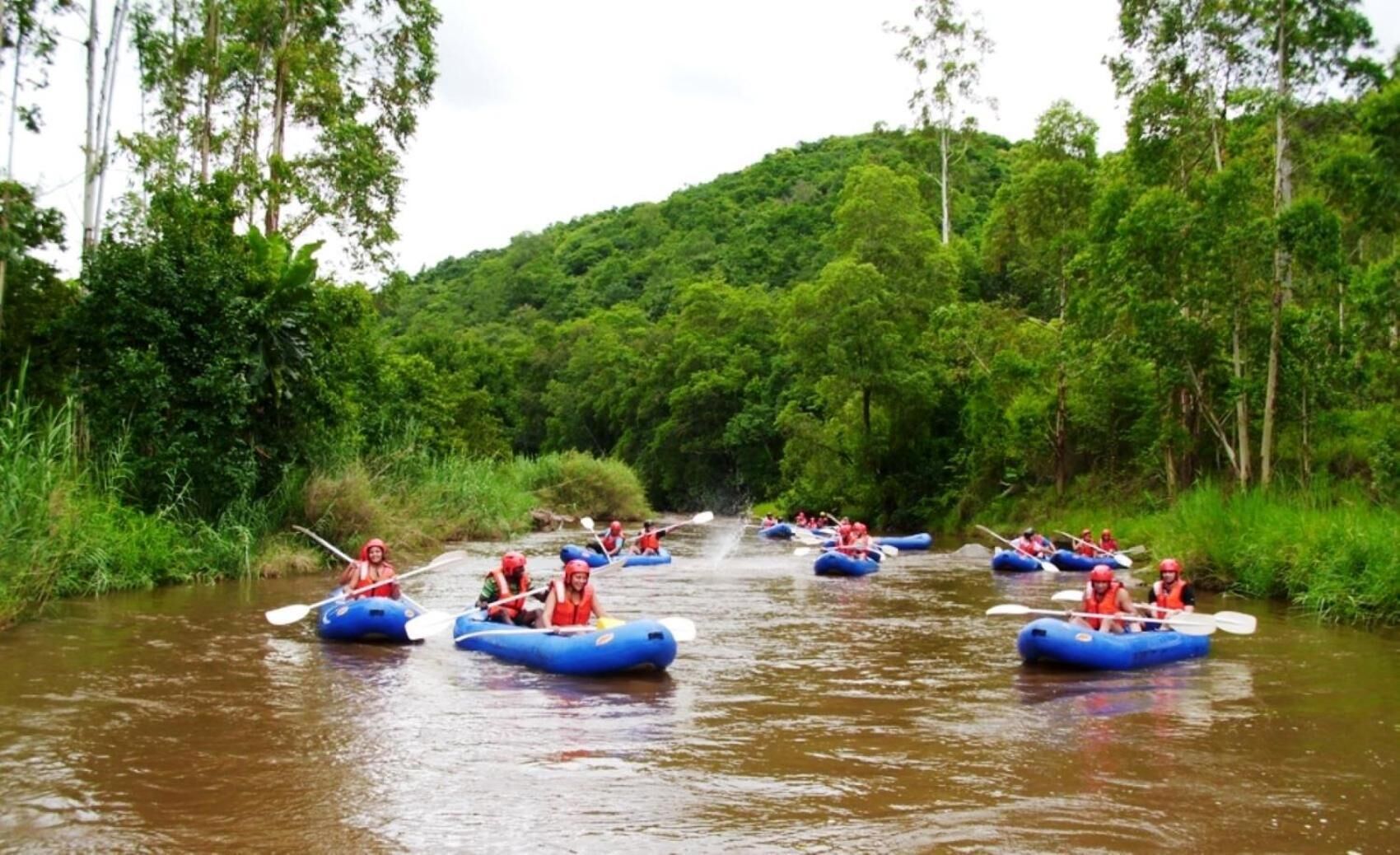 Un grupo de personas en balsas inflables azules flotando en un río rodeado de abundante vegetación.
