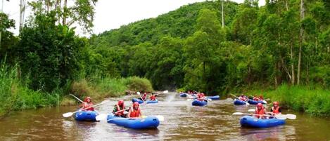 A group of people in blue inflatable rafts on a river surrounded by lush greenery.