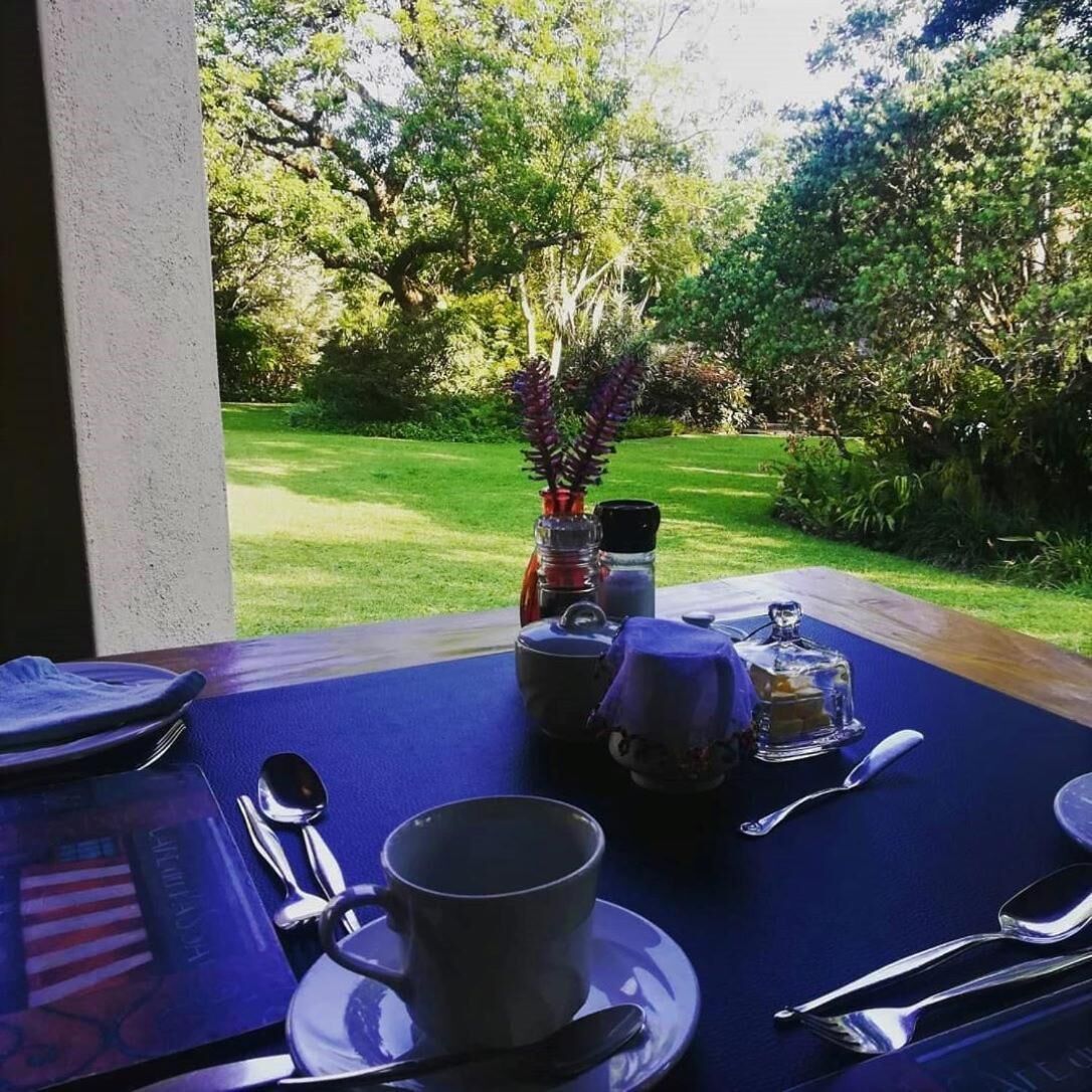 A dining table set with a blue tablecloth, silverware, a cup, and a vase with flowers.