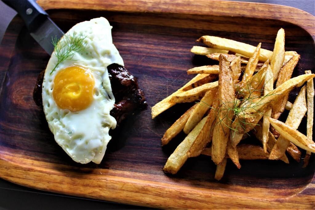 Una tabla de madera con un huevo frito y papas fritas.