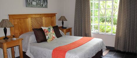 A bedroom with a large bed, two bedside tables with lamps, a window with curtains, and a wall-mounted painting.