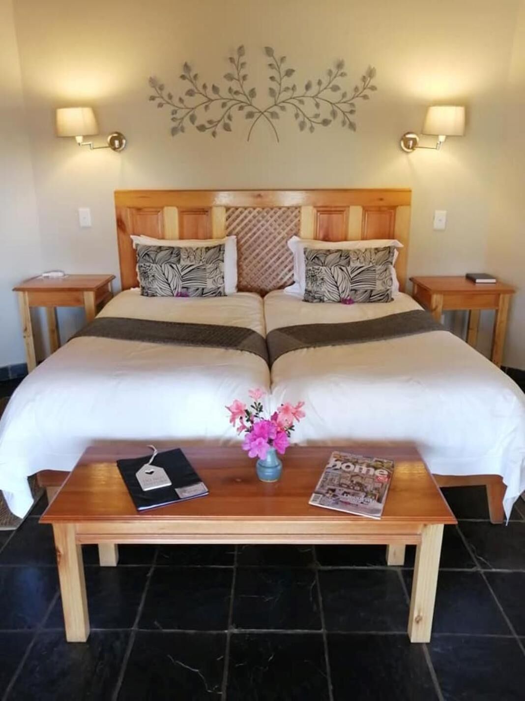 A double bed with a wooden headboard, two bedside tables, a nightstand, a wooden coffee table, a vase with flowers, and a magazine.