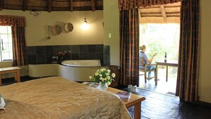 Habitación de hotel con una cama grande, una bañera, una mesa con un florero y vistas al exterior.