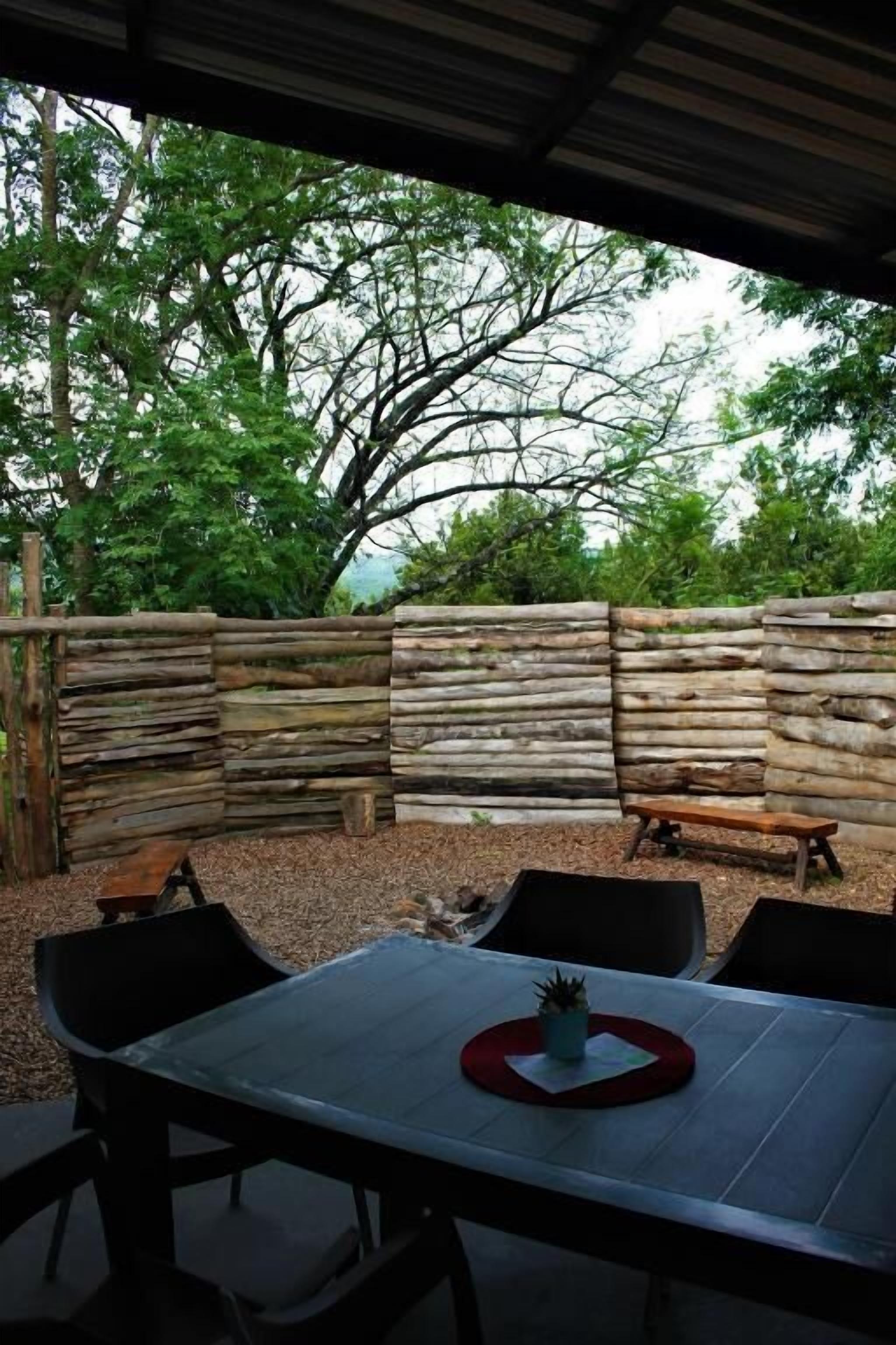 An outdoor patio with a table and chairs, a wooden fence, and trees in the background.