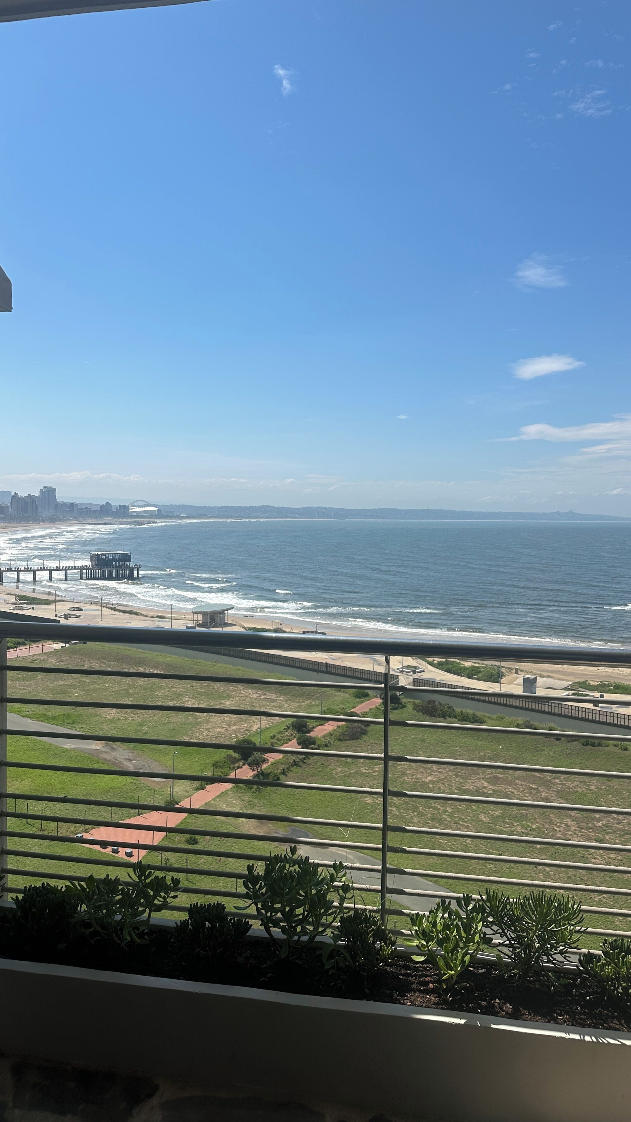 A coastal view with a pier, beach, and distant cityscape.