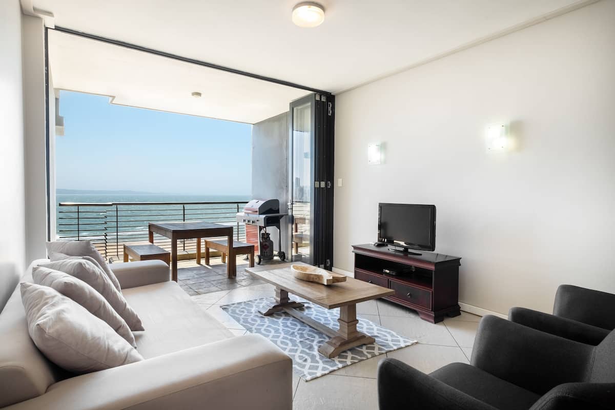 A balcony with a view of the sea, a sofa, a TV, and a grill.