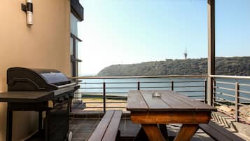 Een terras buiten met een barbecue, picknicktafel en banken, met uitzicht op een waterpartij en een heuvel met een toren.