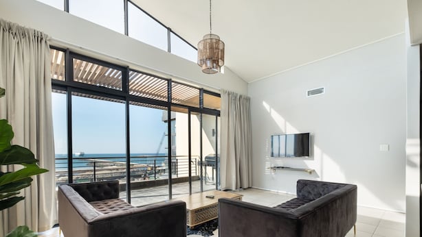 A modern living room with large windows, a flat-screen TV, and two dark sofas. - Point Waterfront Apartments (Durban)
