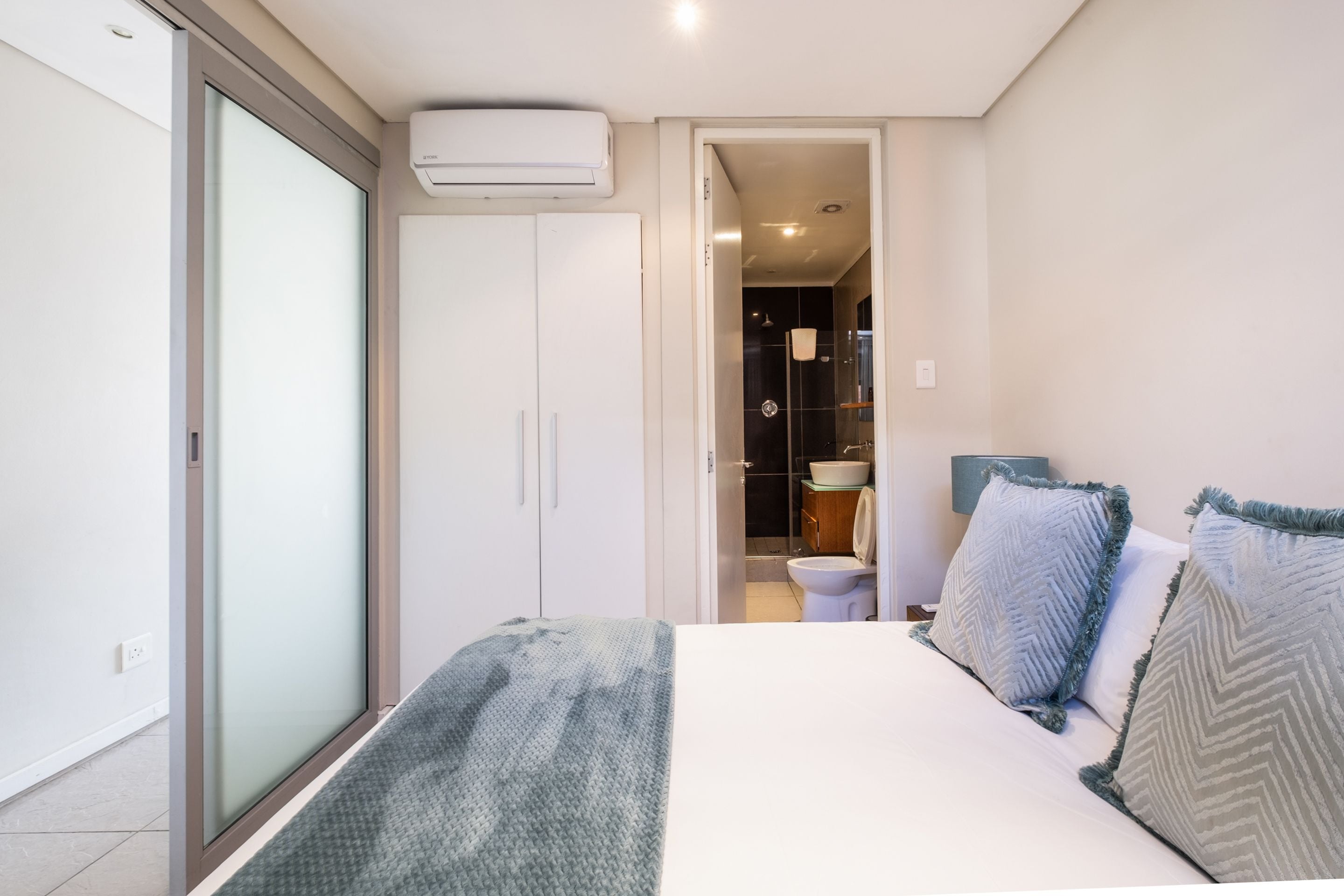 A bedroom with a bed, a wardrobe, and a bathroom visible through an open door.