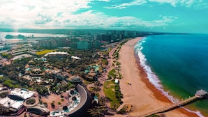 An aerial view of a coastal city with a beach, a cruise ship docked, and a large resort complex with multiple buildings and a curved structure. - Point Waterfront Apartments (Durban)