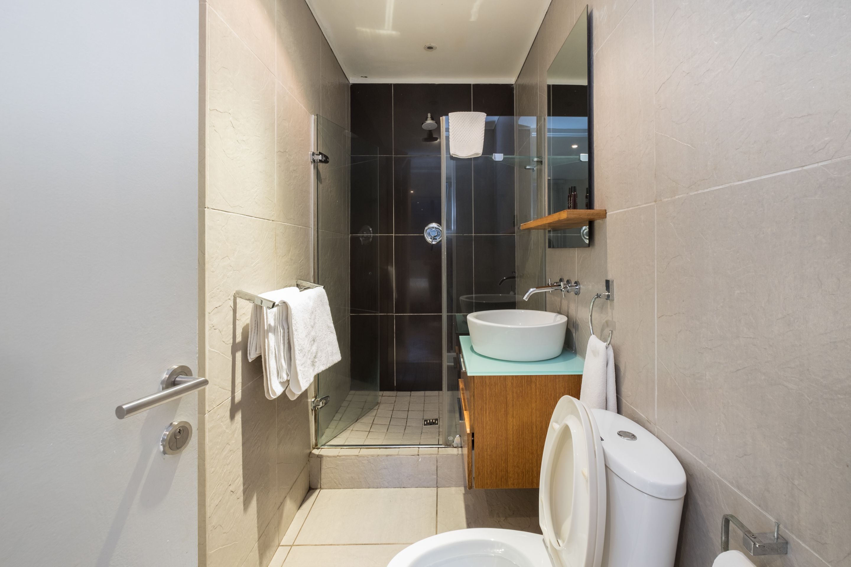 A modern bathroom with a glass shower enclosure, a white sink, and a wooden vanity.