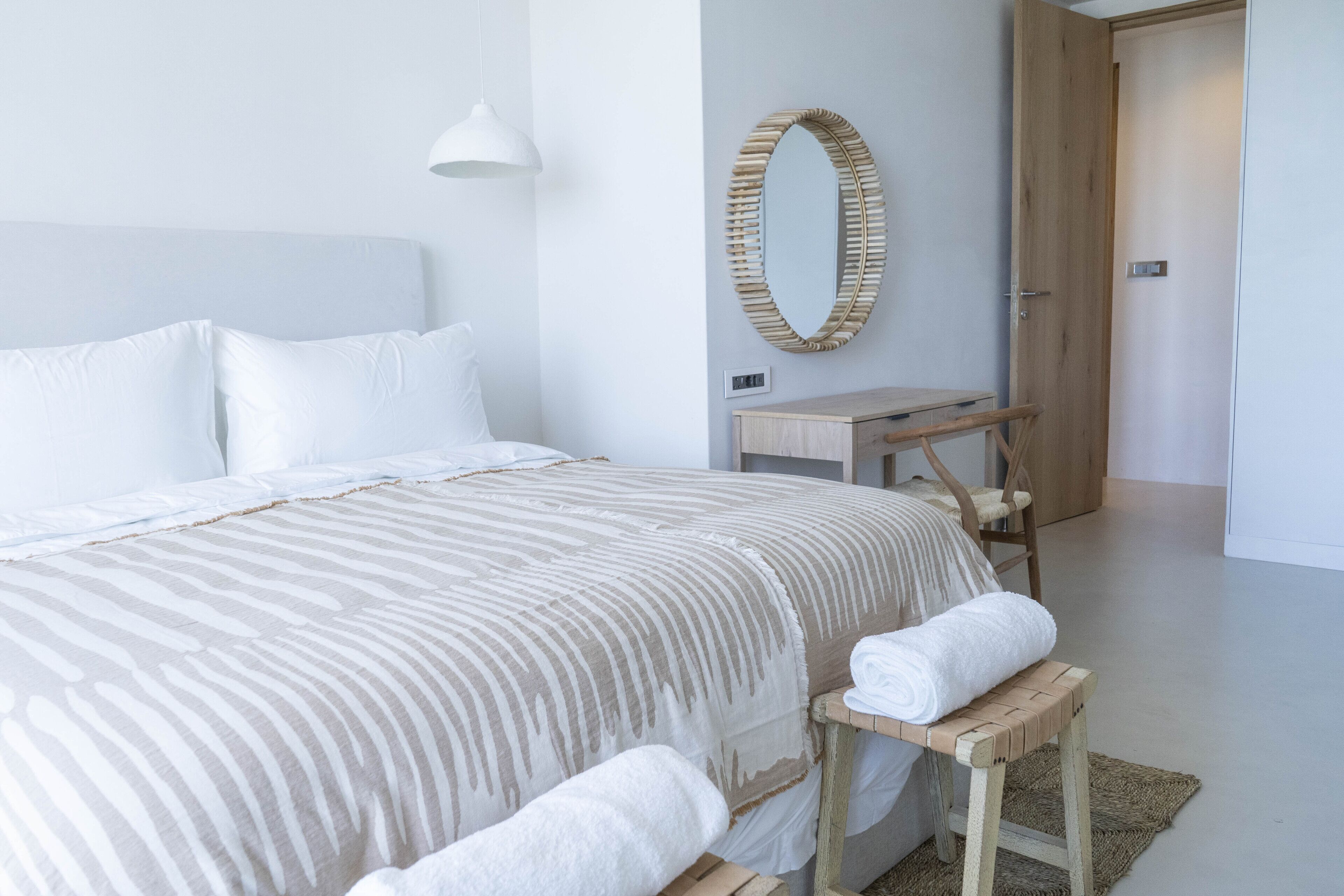 Een slaapkamer met een bed, een houten bankje, een spiegel en een deur.