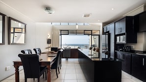 A modern kitchen with black cabinets, a central island, and a dining area with a view of the sea. - Point Waterfront Apartments (Durban)