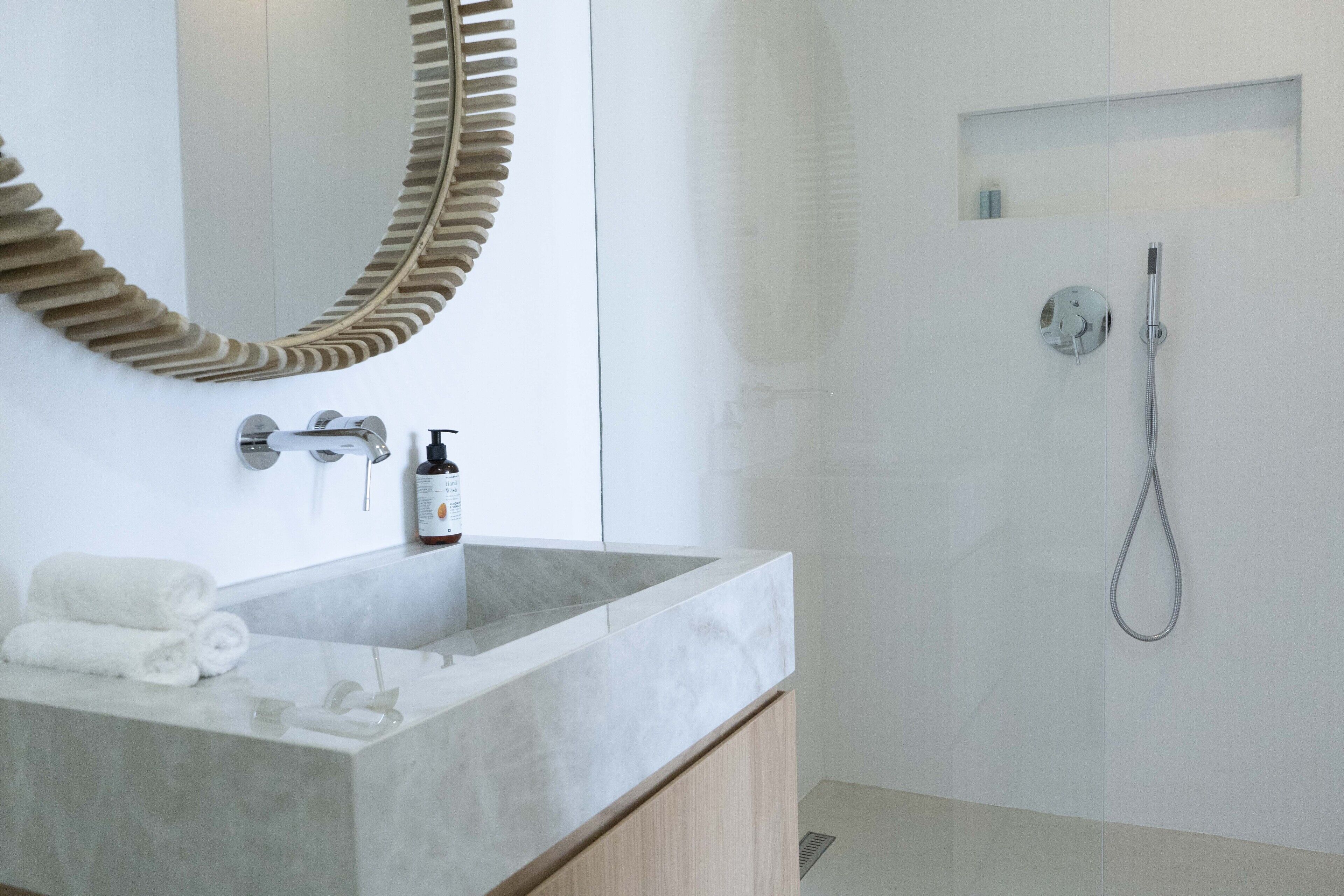 A modern bathroom with a large mirror, a marble sink, and a shower area.