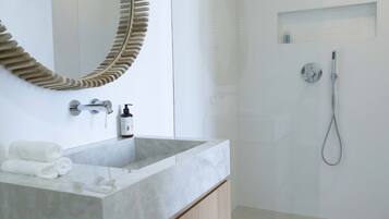 A modern bathroom with a large mirror, a marble sink, and a shower area.