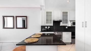 A modern kitchen with white cabinets, a black granite countertop, and a central island with woven baskets.
