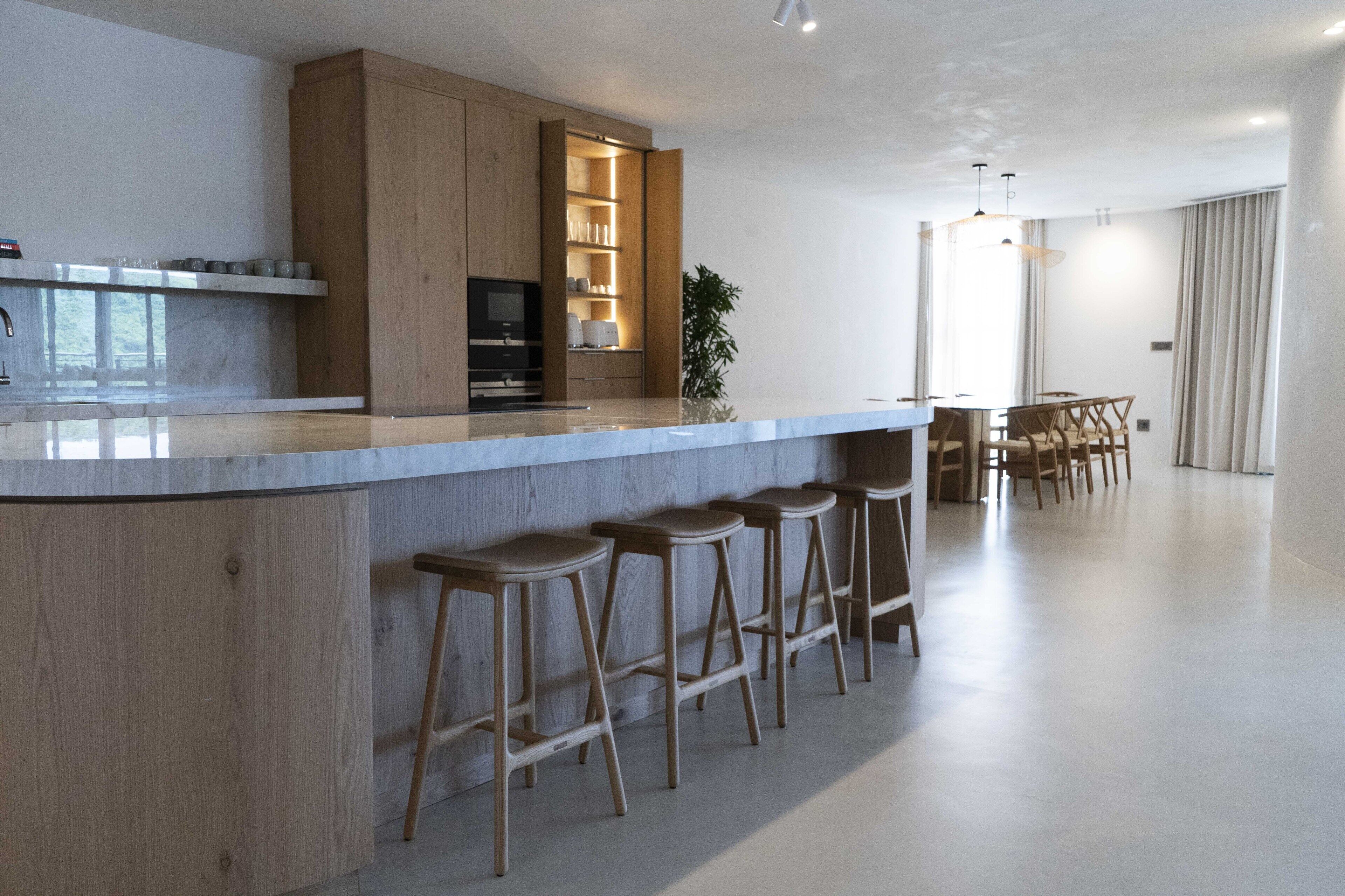 Una cocina moderna con armarios de madera, encimera de mármol y taburetes de bar.
