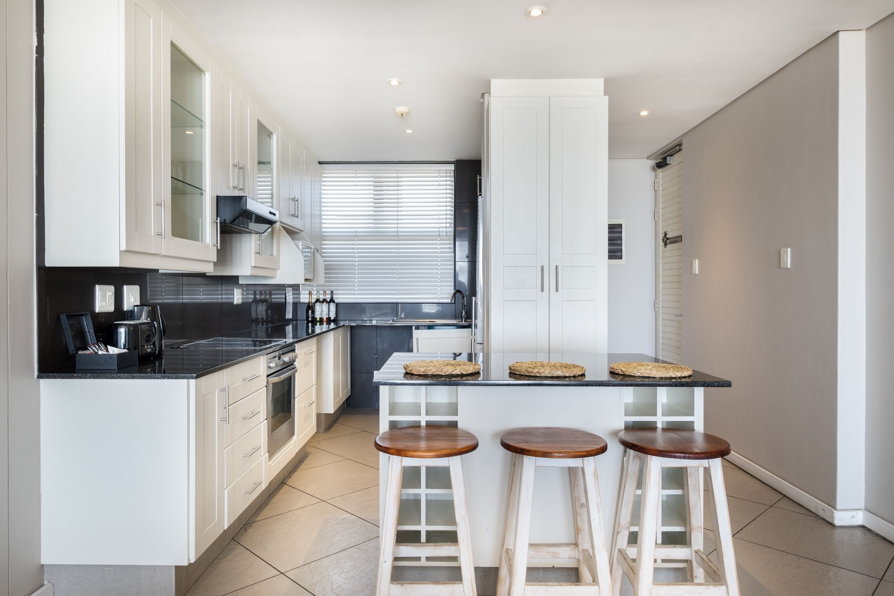 Een moderne keuken met witte kasten, een zwart aanrecht en houten krukken.