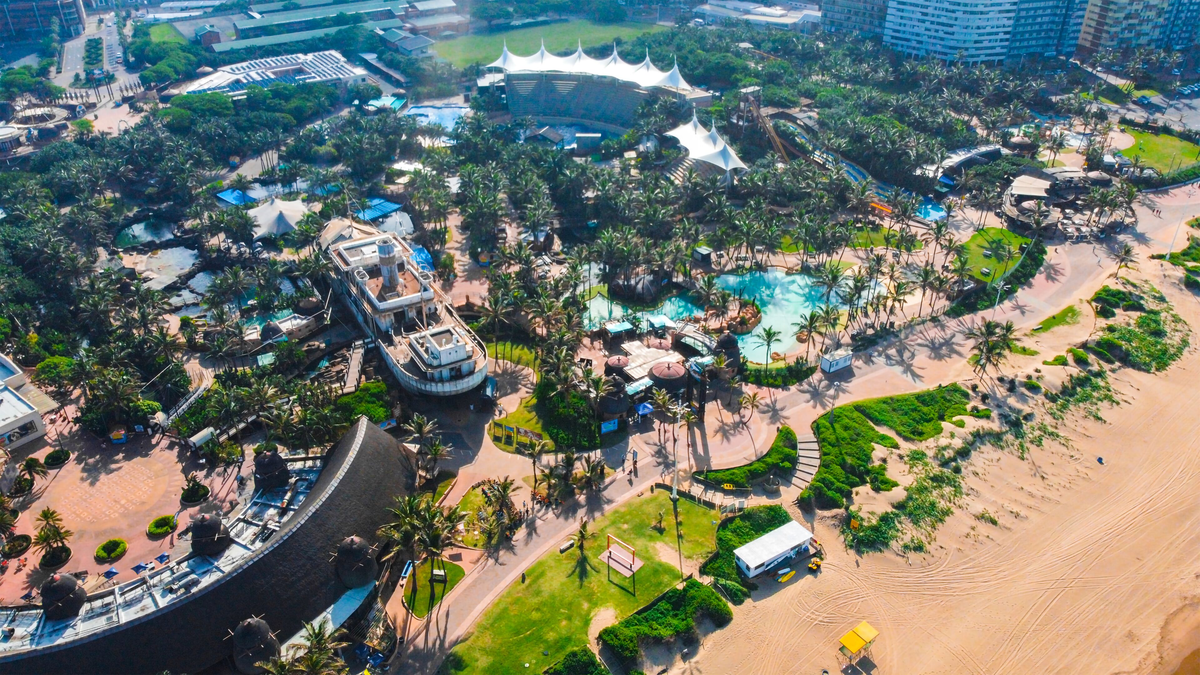 An aerial view of a resort with multiple swimming pools, palm trees, and a beach area.