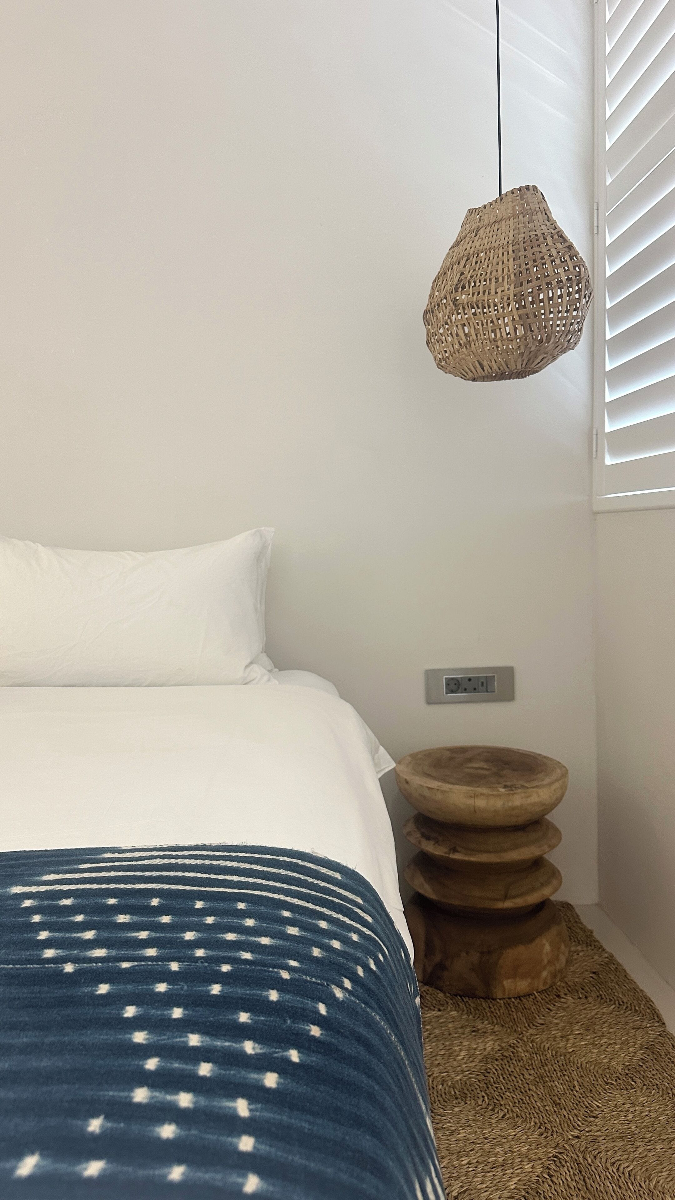 Ein Schlafzimmer mit Bett, einer Hängelampe, einer Steckdose und einem hölzernen Hocker.