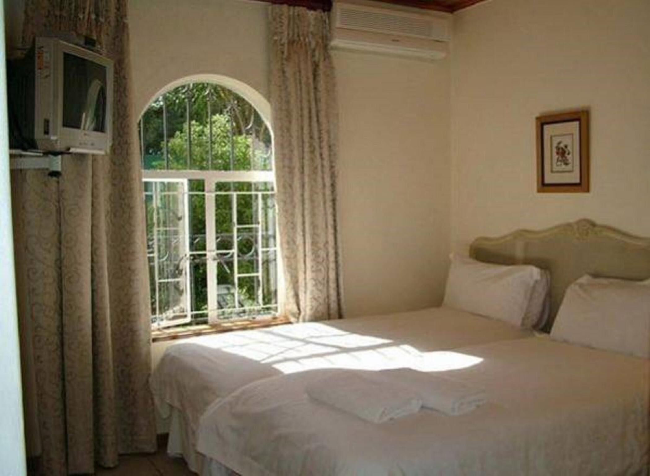 Un dormitorio con cama, ventana con cortinas, un cuadro en la pared y televisor en la pared.