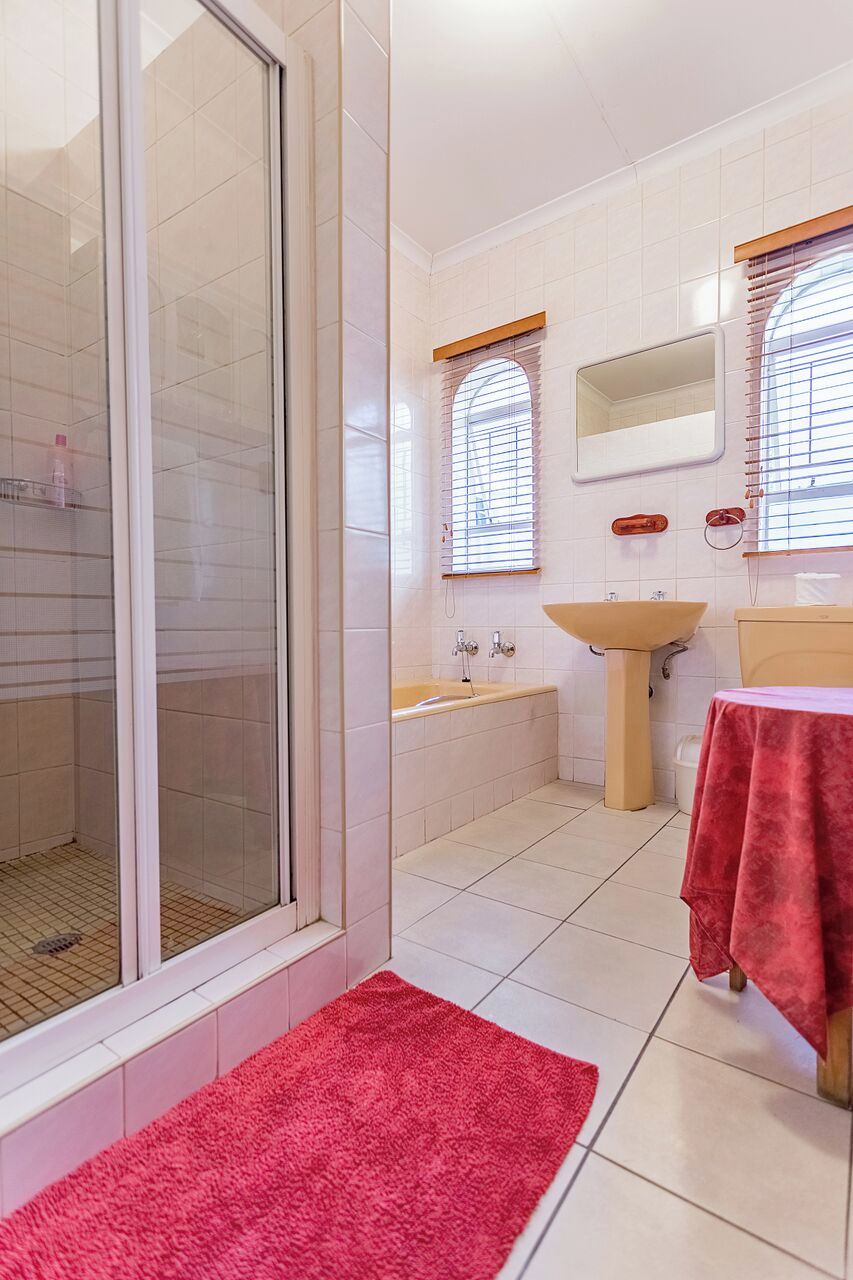A bathroom with a glass shower enclosure, a sink, a mirror, and a red towel on the floor.