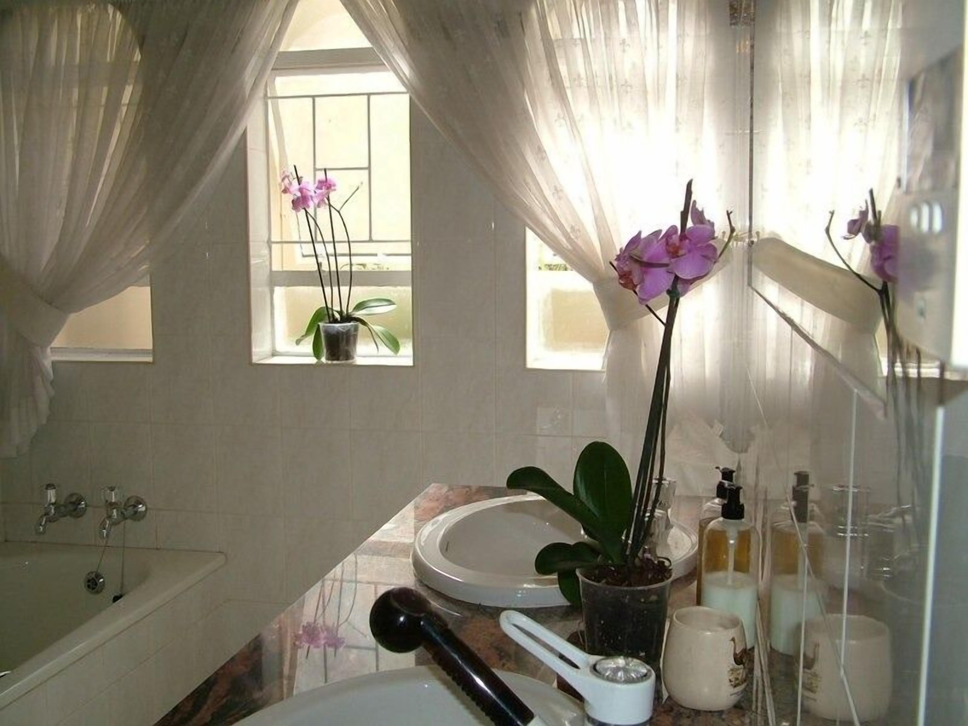 A bathroom with a bathtub, a sink, a window with curtains, and a mirror.