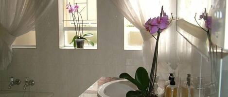 A bathroom with a bathtub, a sink, a window with curtains, and a mirror.