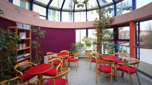Een bibliotheek met boekenkasten, houten stoelen met rode kussens en een glazen plafond.