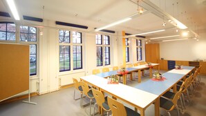 Een congreszaal met lange tafels en stoelen, grote ramen en plafondverlichting.