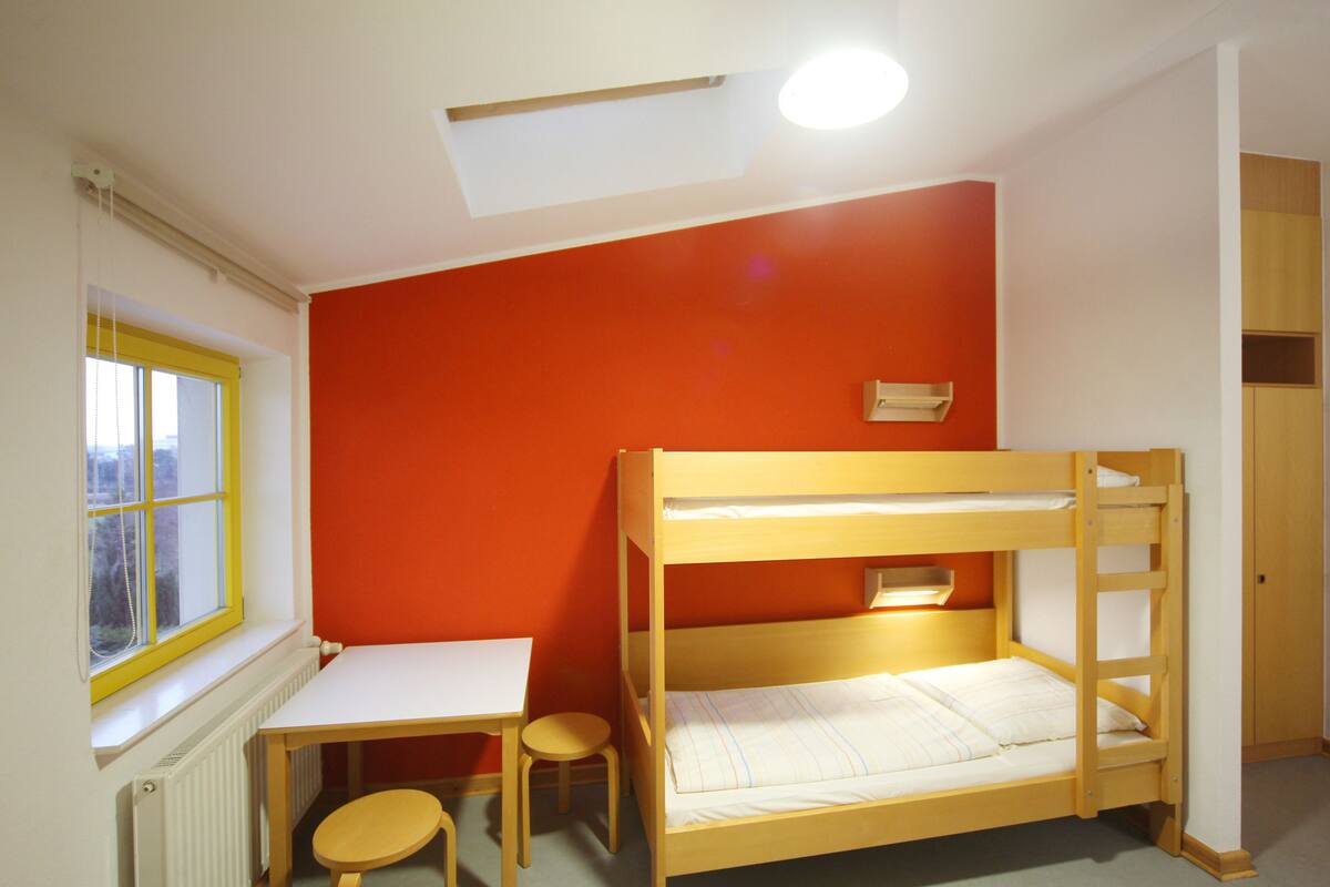 A bunk bed with a desk and chair, a window with yellow blinds, and a red wall.