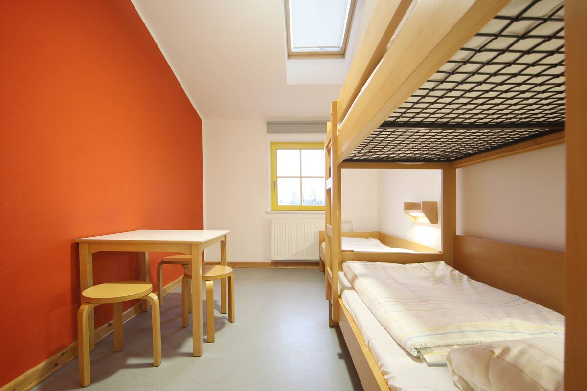 A dormitory room with bunk beds, a desk, and chairs.