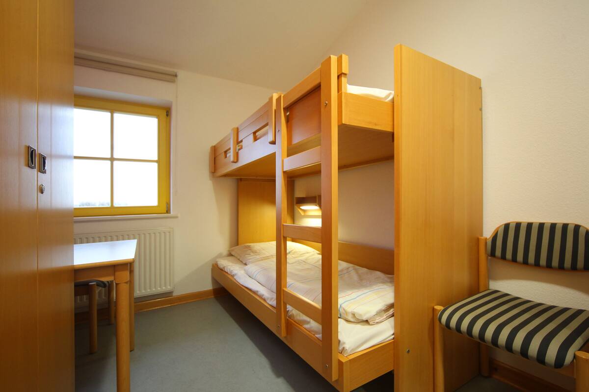 A bunk bed room with a desk and chair, a window, and a radiator.