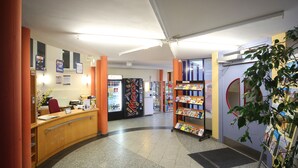 Een receptiegedeelte met een balie, een koelkast, een tijdschriftenrek en een plant.
