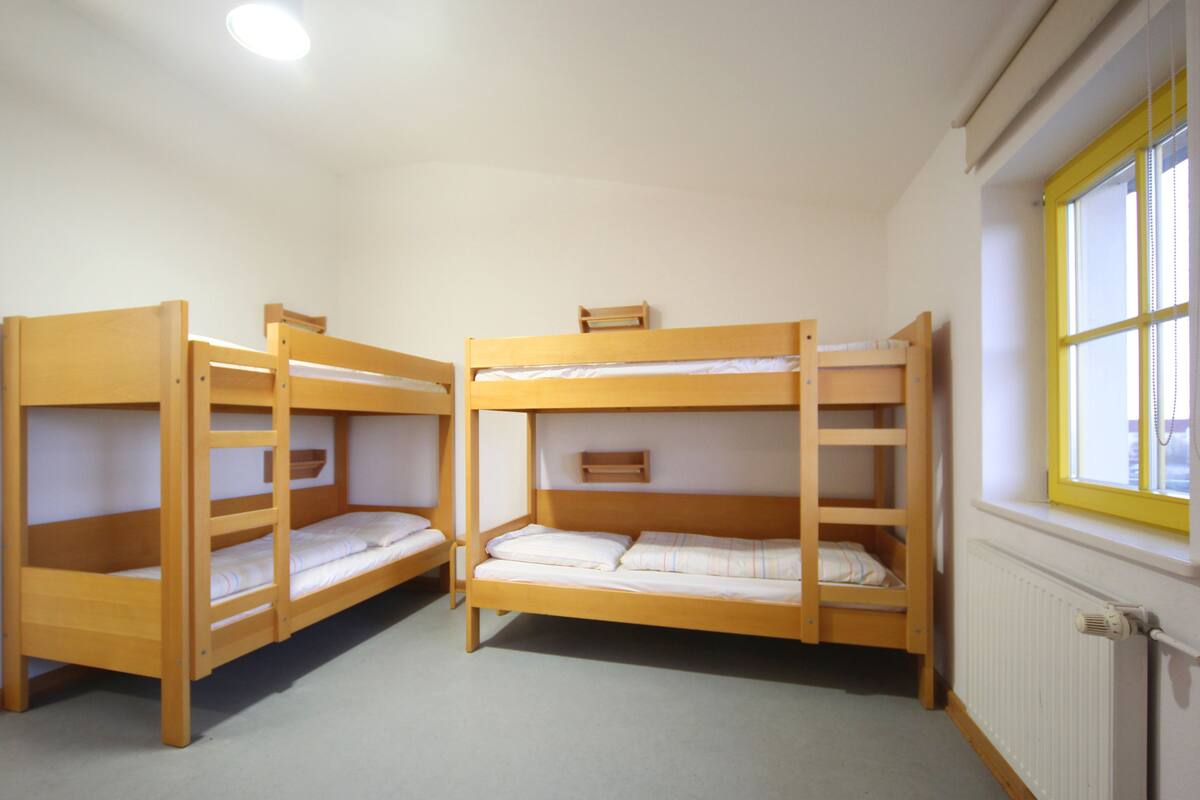 A room with three bunk beds, a window with yellow trim, and a radiator.
