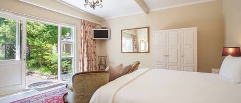 A bedroom with a large bed, a television, a chair, a wardrobe, and a view of greenery outside.