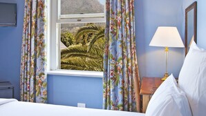 Ein Schlafzimmer mit Bett, Vorhängen, einem Fenster und einer Lampe, mit Blick auf Berge.