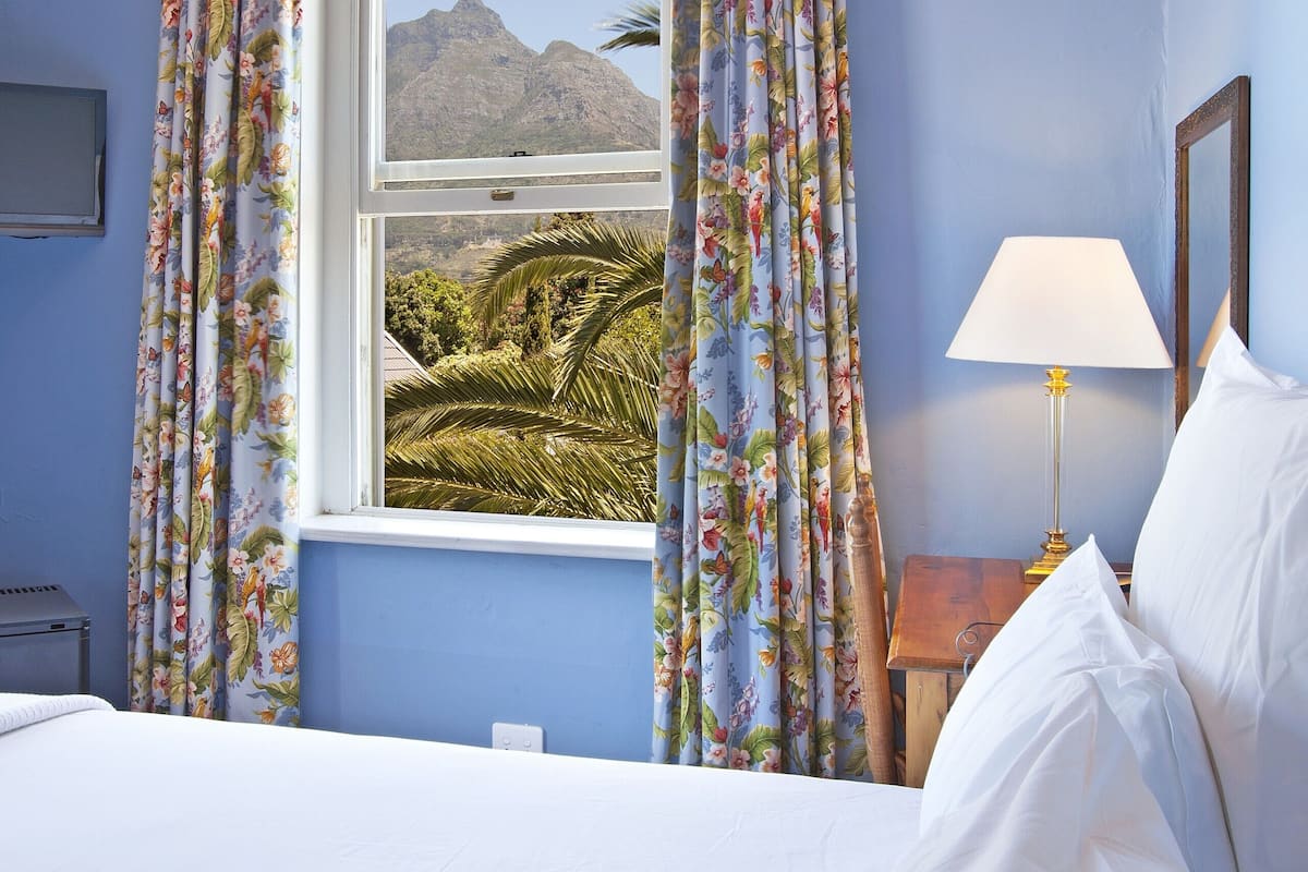 Ein Schlafzimmer mit Bett, Vorhängen, einem Fenster und einer Lampe, mit Blick auf Berge.
