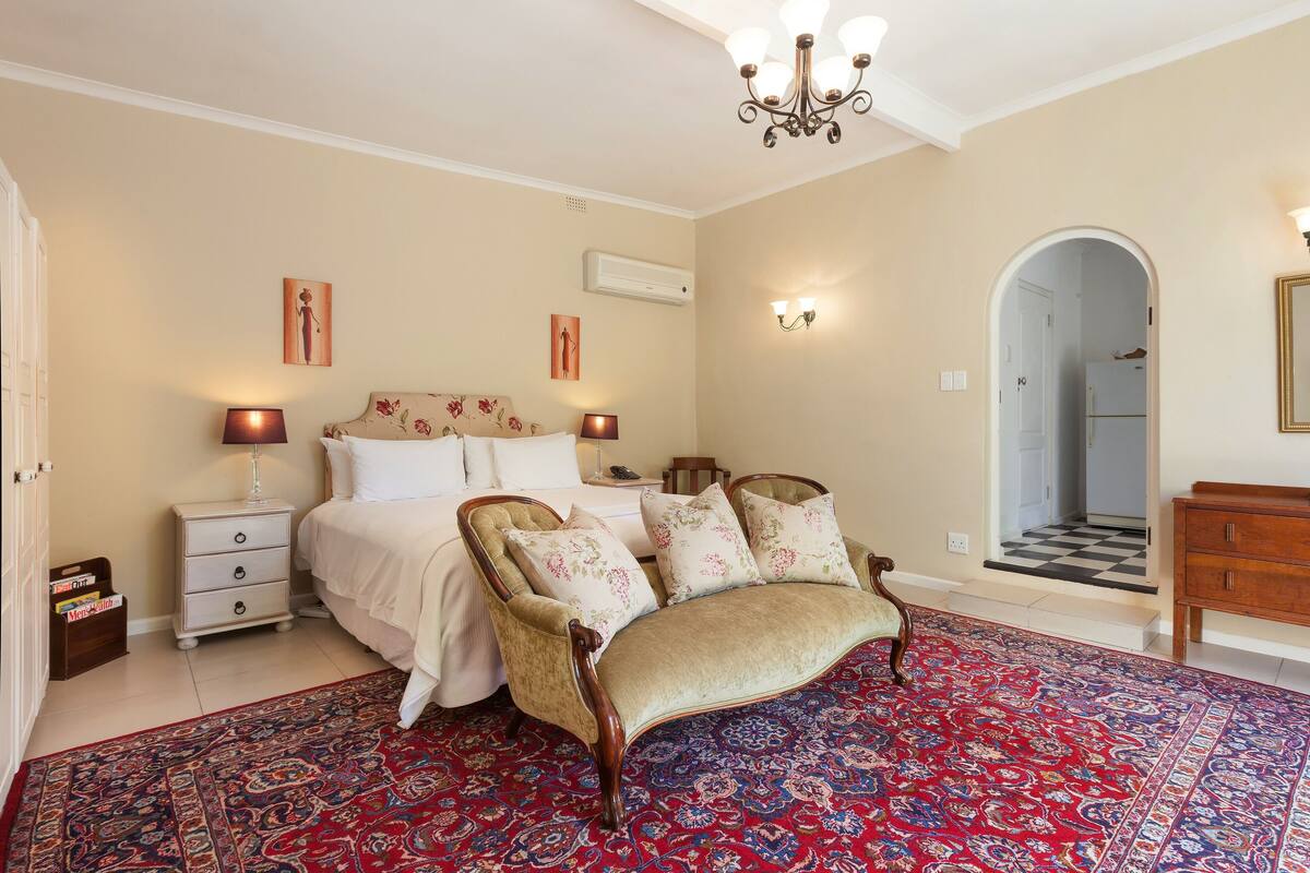 Ein Schlafzimmer mit Bett, Stuhl, Nachttisch, Kommode und einem gemusterten Teppich.