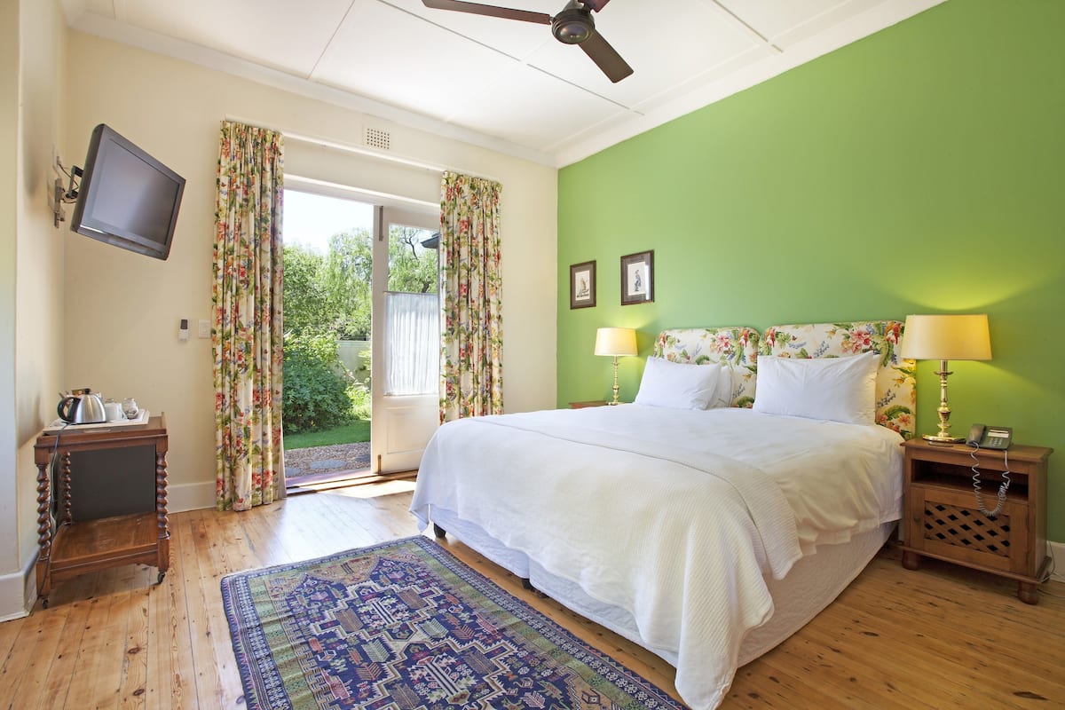 Ein Schlafzimmer mit einem Bett, zwei Nachttischlampen, einem Nachttisch, einem an der Wand befestigten Fernseher und einem gemusterten Teppich.