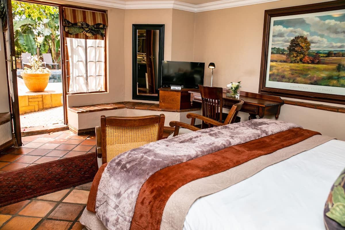 A hotel room with a large bed, a television, a desk with a chair, and a painting on the wall.