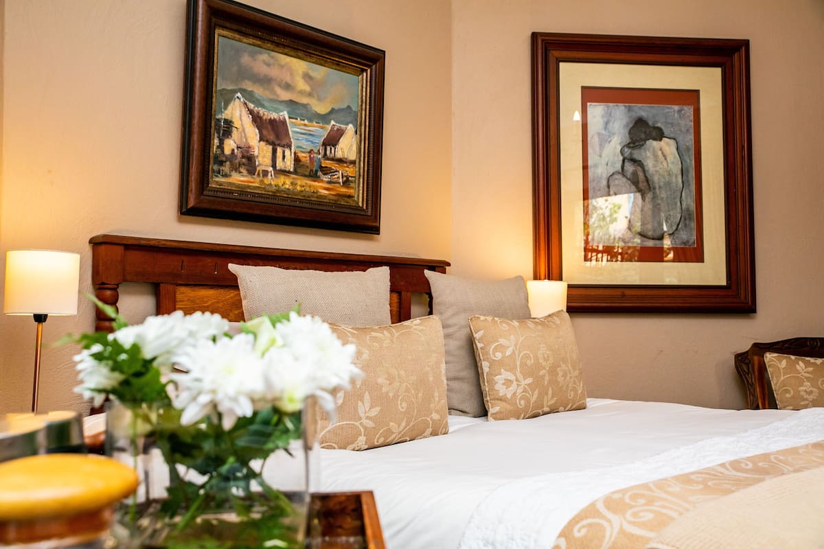 A hotel room with a large bed, two bedside lamps, a vase with flowers, and two framed artworks on the wall.