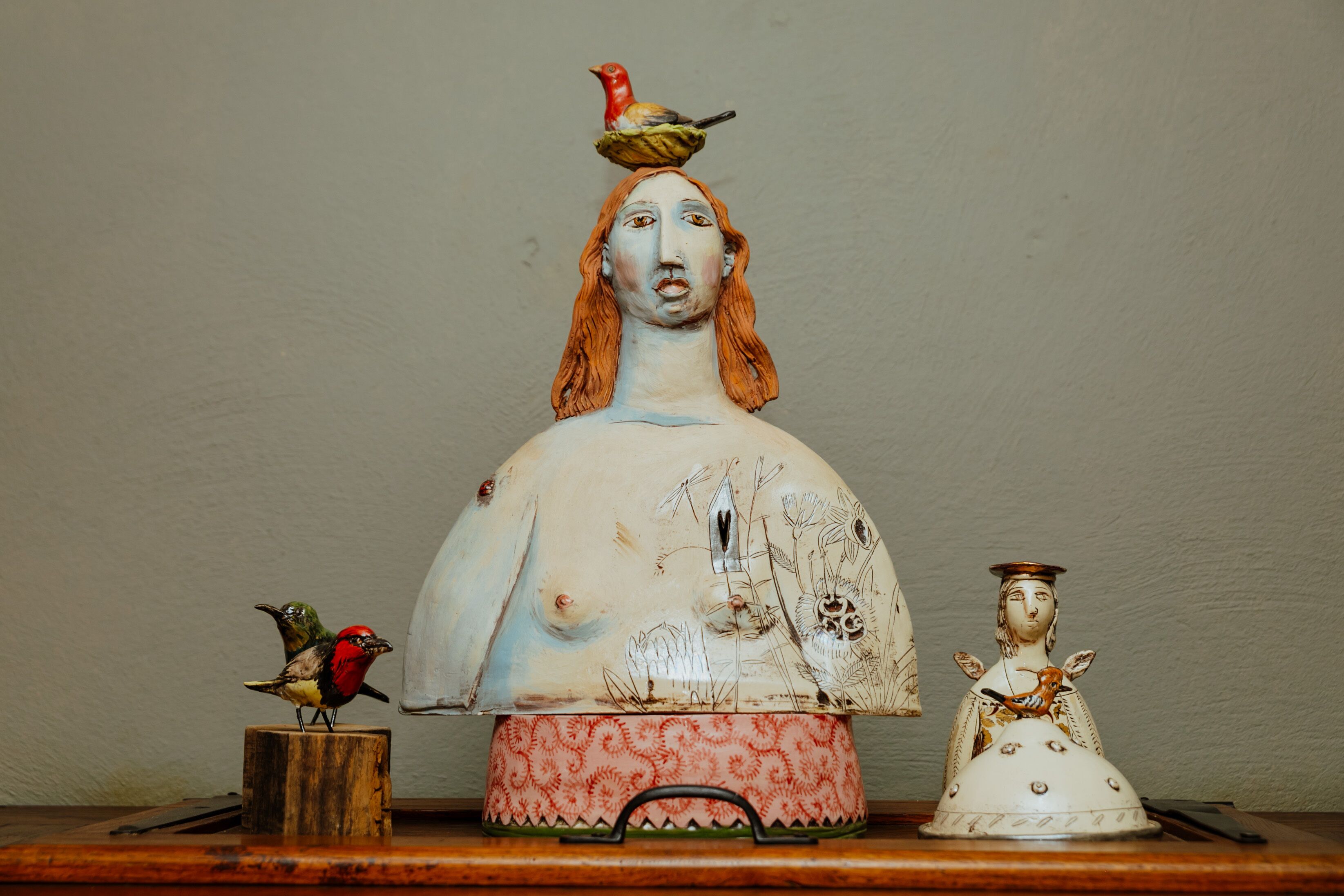 Una escultura de cerámica con un pájaro en la parte superior, un pájaro más pequeño sobre un pedestal y una figurita.
