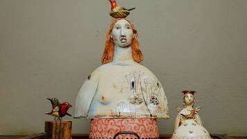 Una escultura de cerámica con un pájaro en la parte superior, un pájaro más pequeño sobre un pedestal y una figurita.