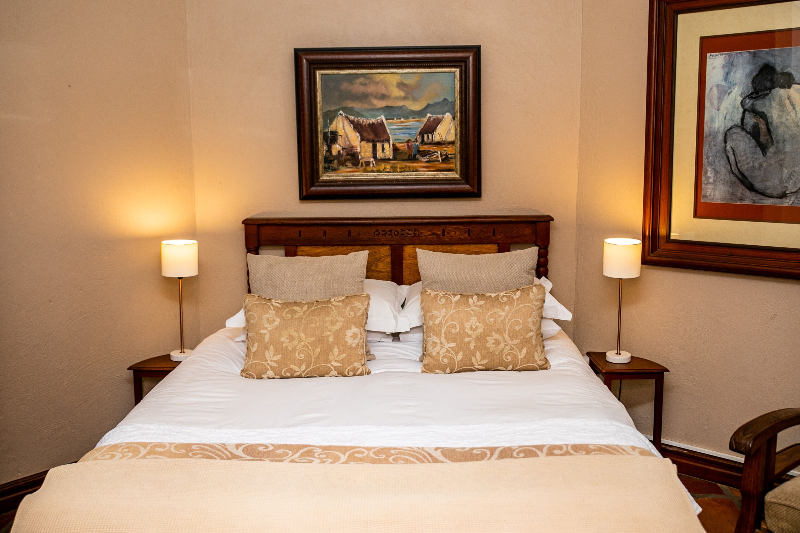 A neatly made bed with a headboard, two bedside tables with lamps, and two framed artworks on the walls.