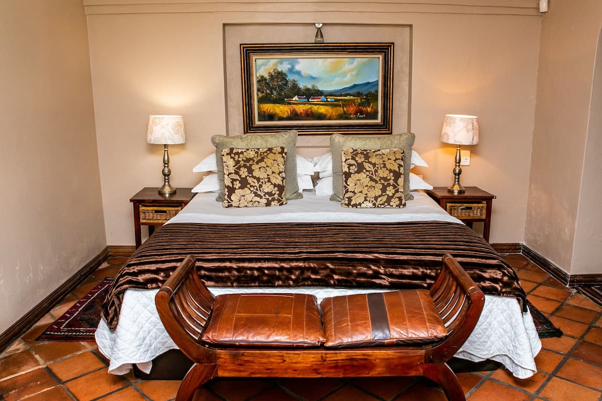 A bedroom with a large bed, two bedside tables with lamps, a wooden bench, and a painting on the wall.