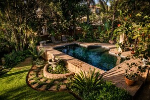 A pool surrounded by lush greenery, with a stone fountain and seating area.