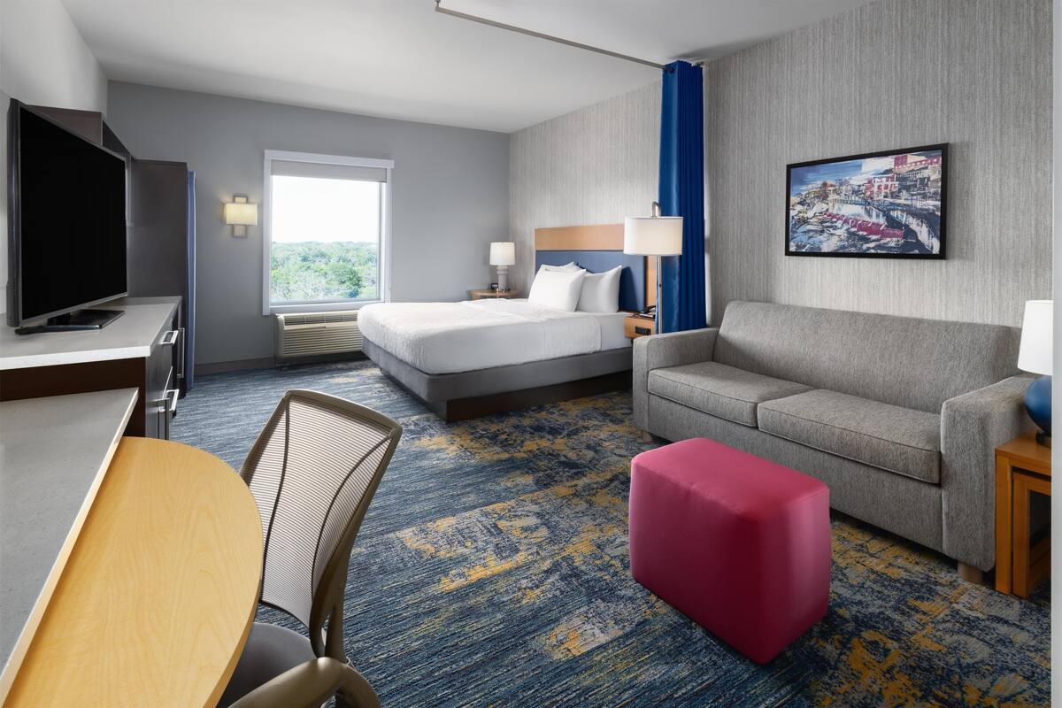 A hotel room with a bed, a sofa, a TV, a desk, and a chair.