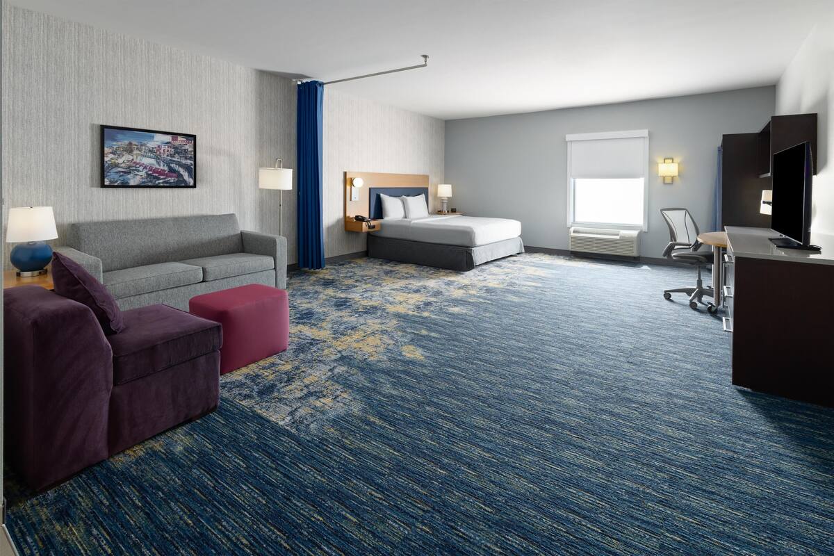 A hotel room with a bed, a sofa, a desk, and a TV.