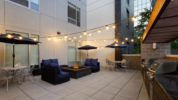 Un patio al aire libre con mobiliario, una chimenea, luces colgantes y una zona de parrilla.